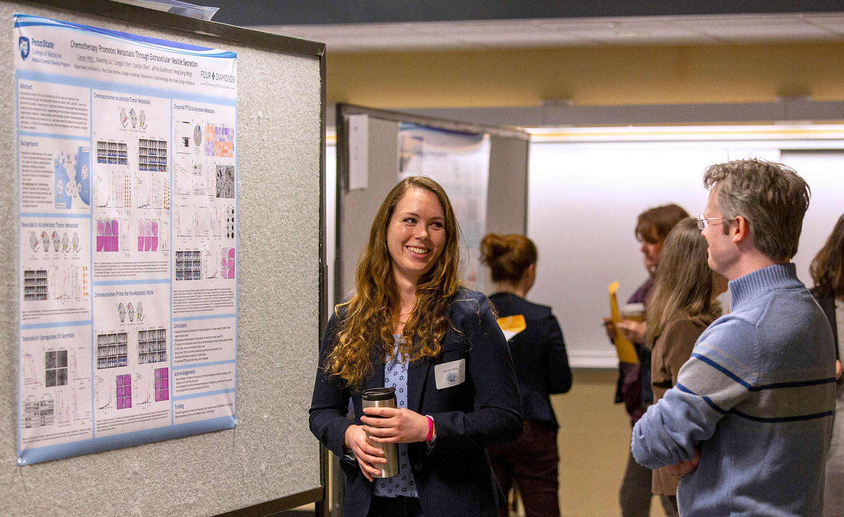 A woman stands near an academic poster, talking and smiling to another person.