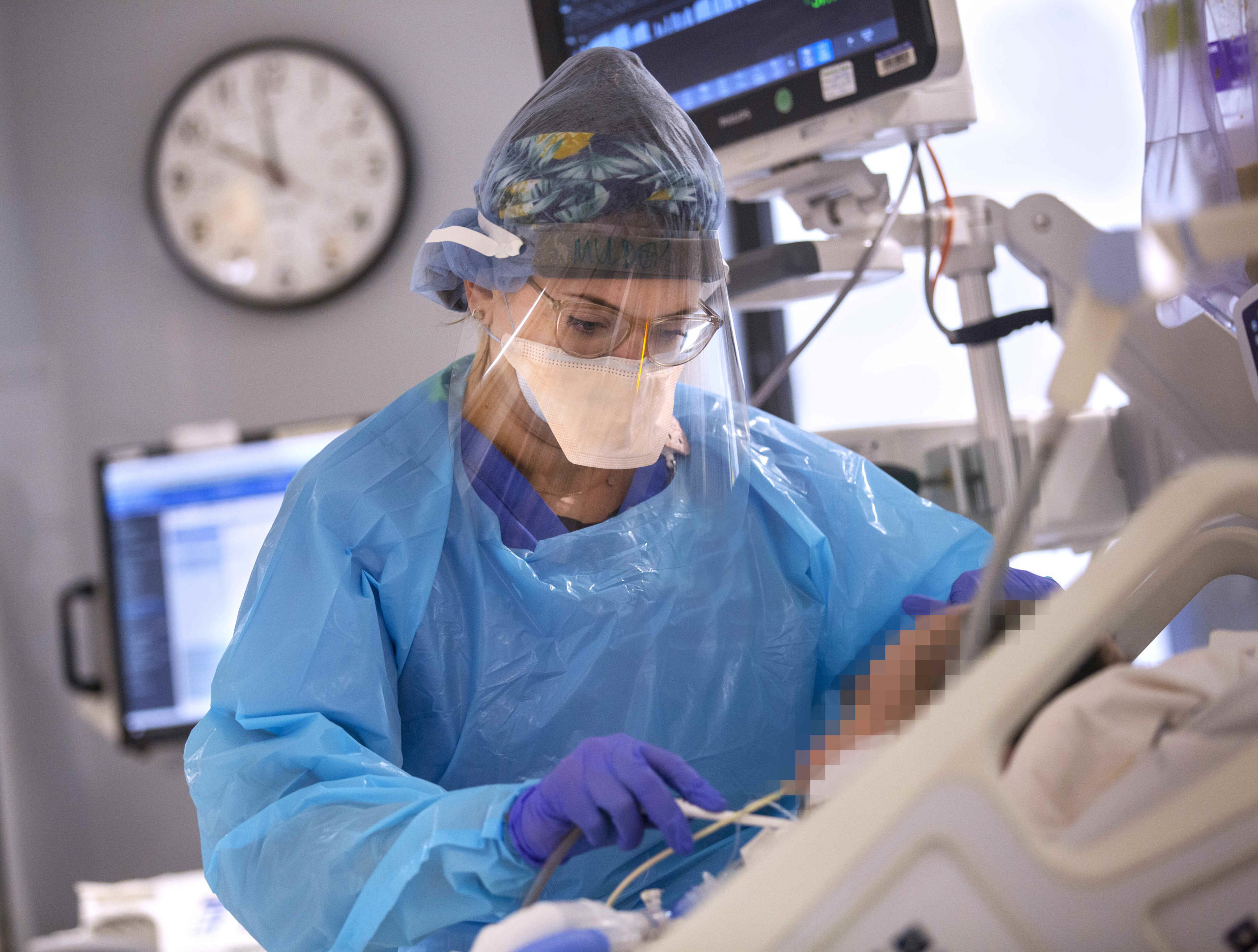 A nurse in personal protective equipment cares for a patient in a hospital bed