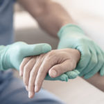 A pair of gloved hands holding another hand without a glove, in a hospital setting.