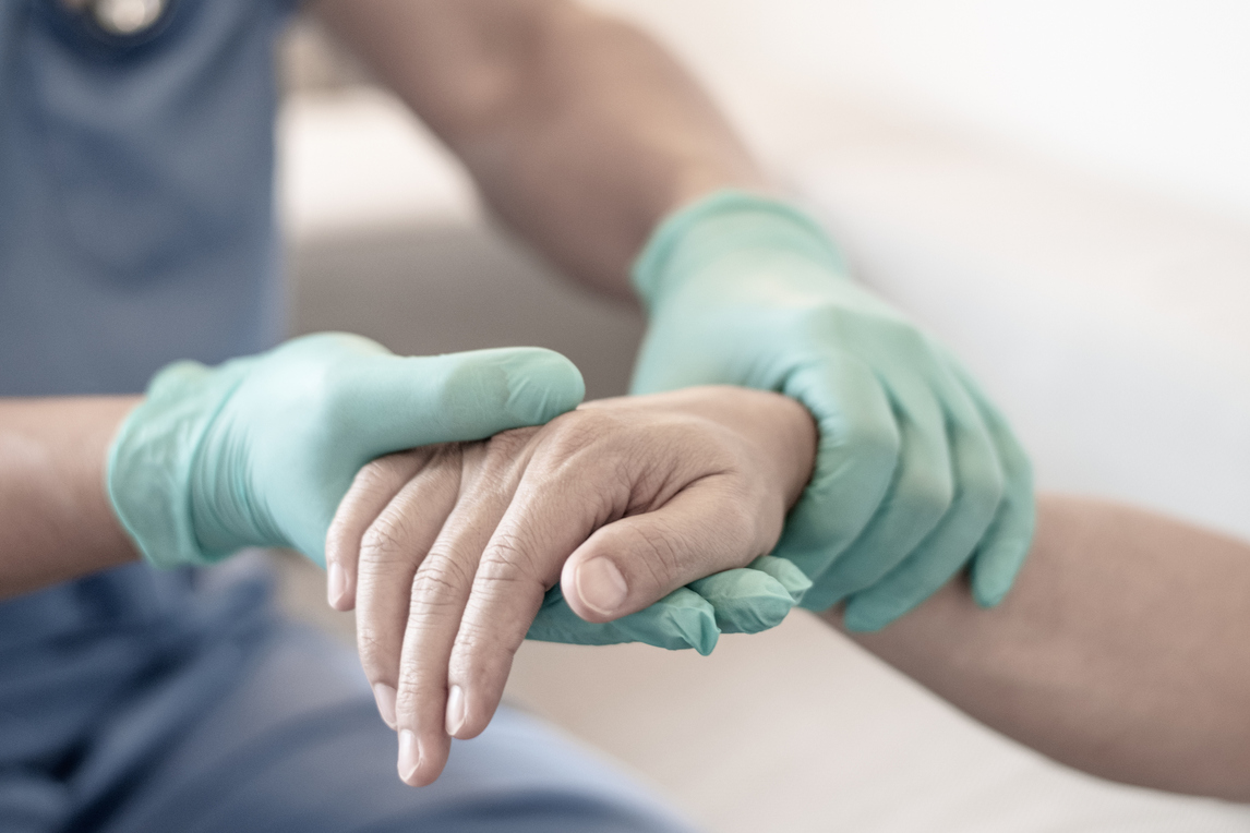 A pair of gloved hands holding another hand without a glove, in a hospital setting.