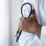 Close-up of doctor’s coat with hand holding a stethoscope.