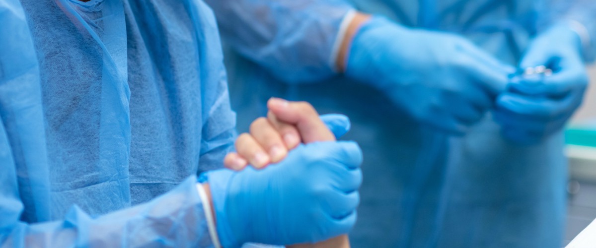 The rubber gloved hand of a health care worker is shown holding the hand of a patient.