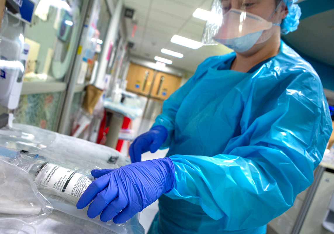 A nurse dressed in personal protective equipment prepares a medication