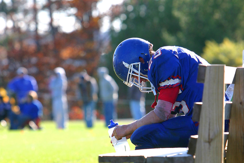 A high school football player sits on bench during game looking down at his water bottle in this stock image.