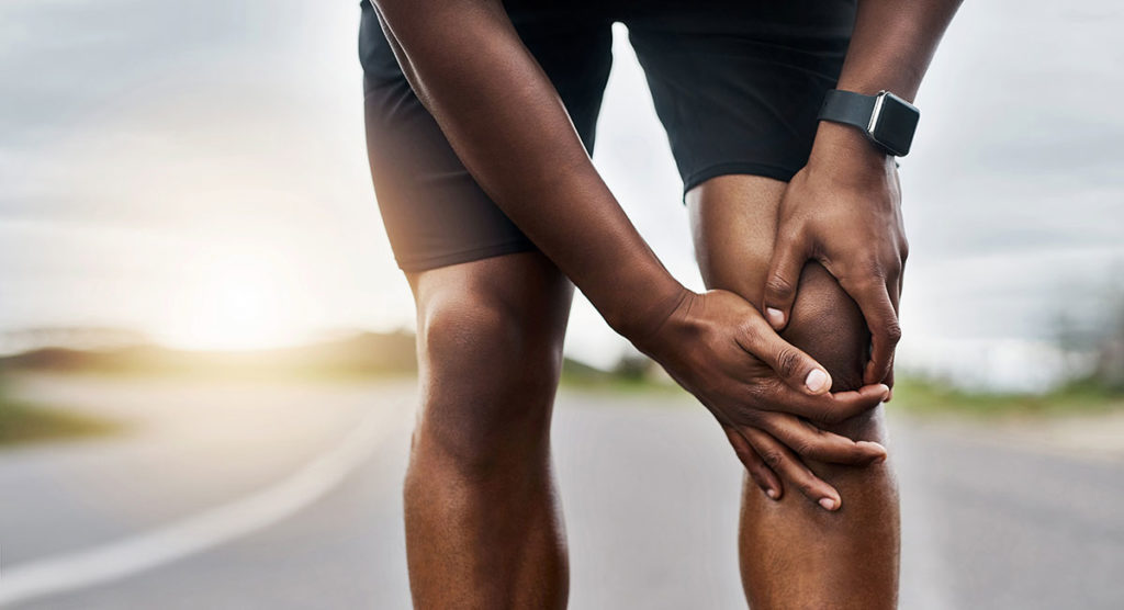 A runner braces his left knee with his hands while stopped on the road in this stock image.