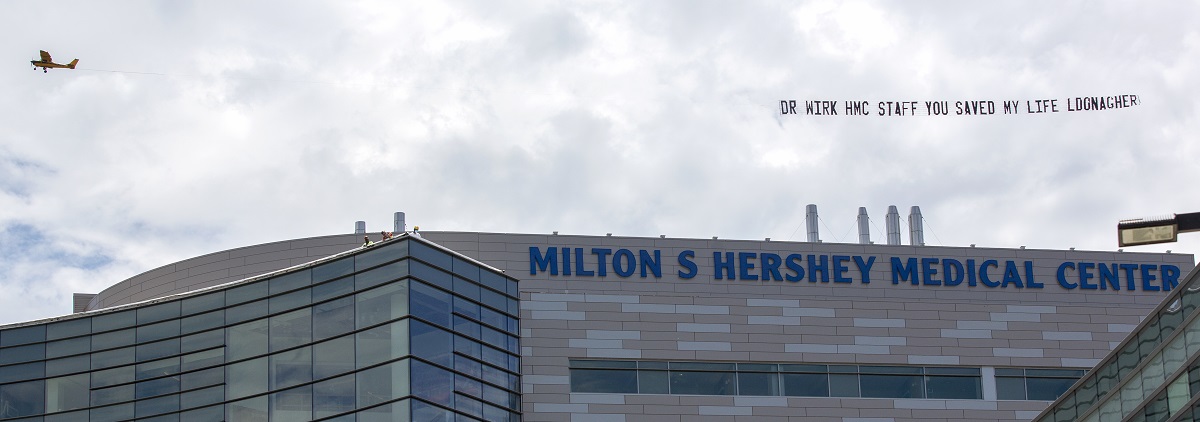 A plane flies in the sky above Hershey Medical Center, trailing a banner.