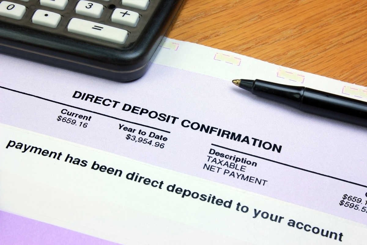 The image shows a calculator and a pen atop a form marked “Direct Deposit Confirmation.” The form is sitting on a woodgrain surface.