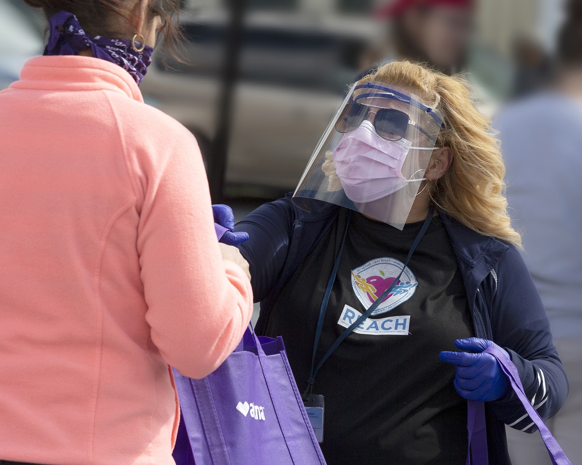 Madeline Bermudez, wearing mask, face shield and sunglasses, hands a bag to a woman wearing a mask.