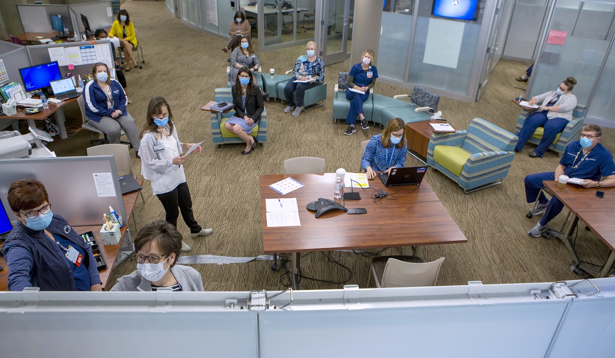 A group of 11 women and one man wearing masks sit in a library during a meeting of the Hershey Incident Command Center on May 21. They are facing a white board.