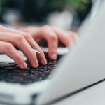 Two hands type on an opened laptop. The IS portal service icon, a red and white circle, is on the right.