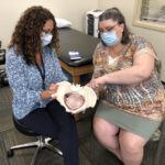 Pelvic floor physical therapist Margaret Homan, left, holds a model pelvis in her hands as she discusses with Pamela Betz how therapy improves symptoms of pelvic floor dysfunction. They both are seated and wearing face masks.