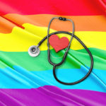 A stethoscope circles a red heart on top of a flag with the colors, from top: red, orange, yellow, green and blue.
