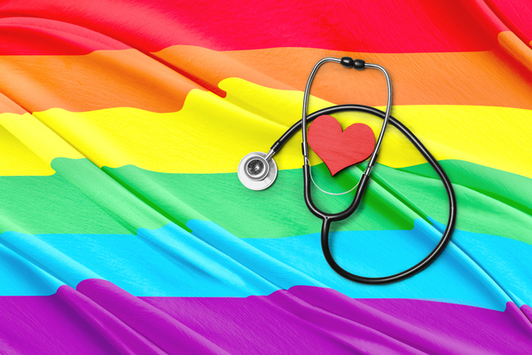 A stethoscope circles a red heart on top of a flag with the colors, from top: red, orange, yellow, green and blue.