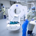 Three workers dressed in protective clothing and wearing face masks, gloves, shoe and head covers, sanitize a CT scan room after it was used to check a COVID-19 patient at St. Joseph Medical Center.