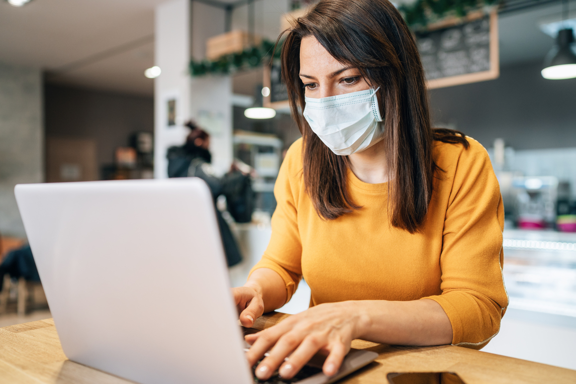 A woman in a face mask is sitting at a desk using a laptop.