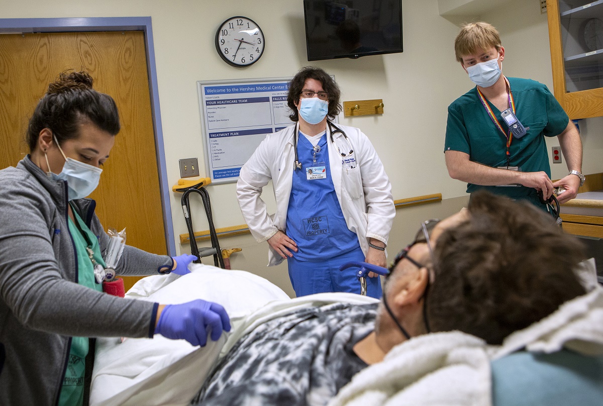 Three people wearing scrubs and face masks surround a patient. Fourth-year medical student Gregory Vece is in the center.