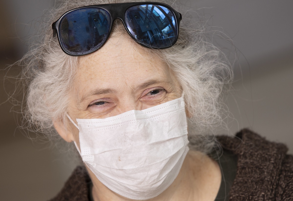 An older woman smiles behind a face mask. Her sunglasses rest on top of her head.