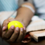 An outstretched arm holds a ball in the palm of a hand during blood collection.
