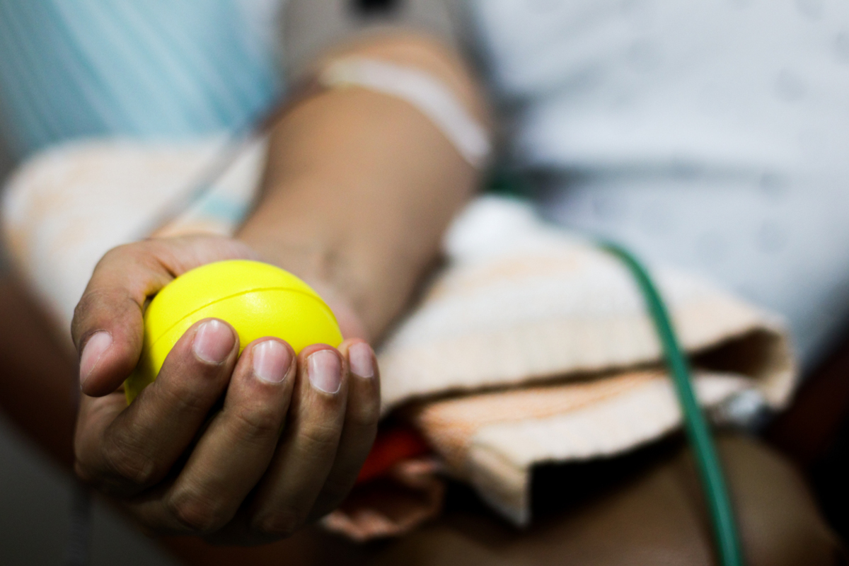 An outstretched arm holds a ball in the palm of a hand during blood collection.
