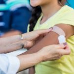 Female doctor applies an adhesive bandage to a woman’s arm after the woman receives a flu shot.