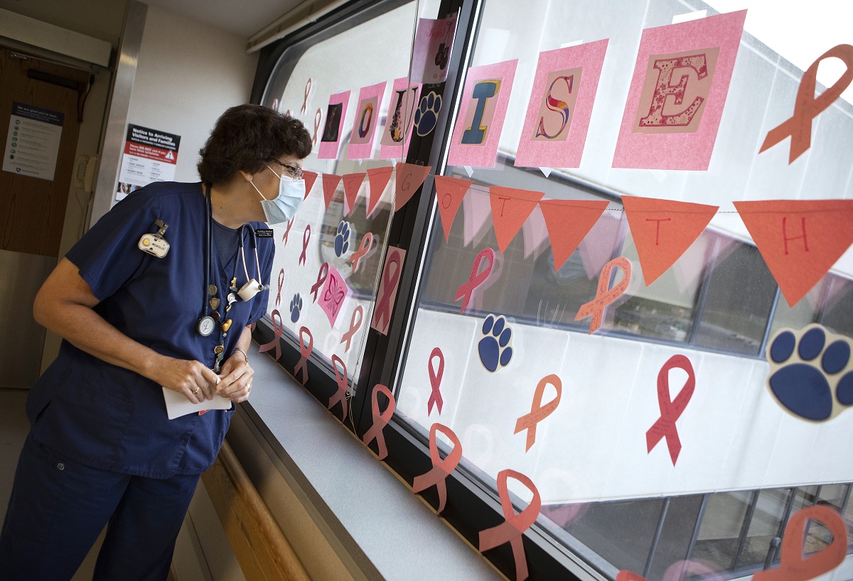 Louise Kline, wearing a mask and scrubs, examines a window upon which are construction-paper decorations. The name Louise is spelled out in big letters.