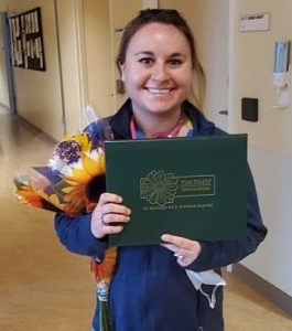 Rachel Drzewicki holds flowers and a plaque in a hallway and smiles.