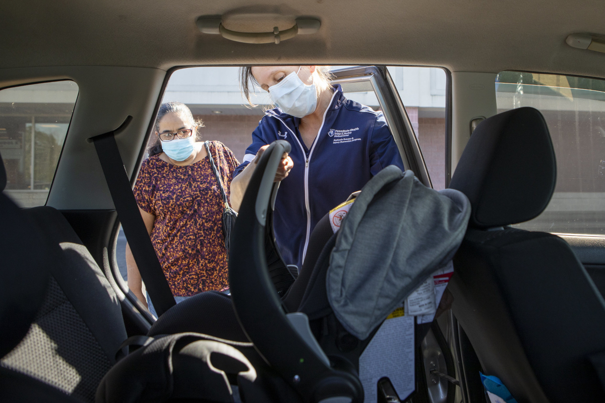 Two women stand outside of a car, looking in at an infant seat in the back seat.