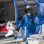 Two workers dressed in flight jumpsuits and wearing helmets and masks remove a litter from a Life Lion helicopter.