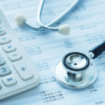 A stethoscope and a calculator rest on a paper with mathematical figures on it.