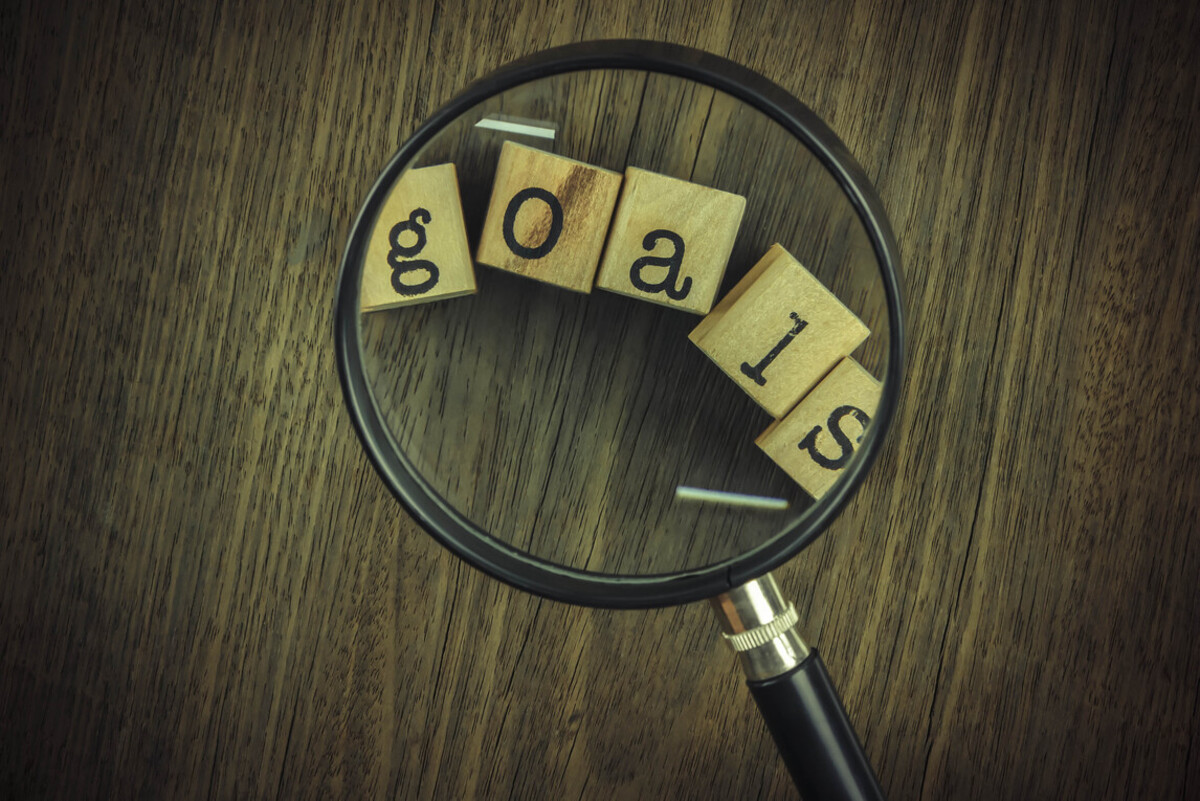 A magnifying glass focuses on wooden tiles that spell out the word “goals.”
