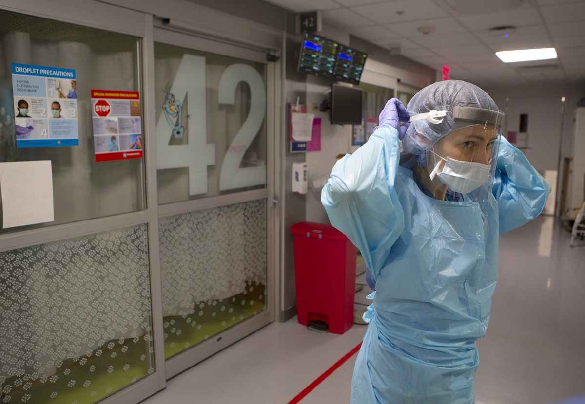 Dr. Jennifer Cooper puts on a face shield, mask, gown and rubber gloves. Behind her, decals pepper a sliding glass door.