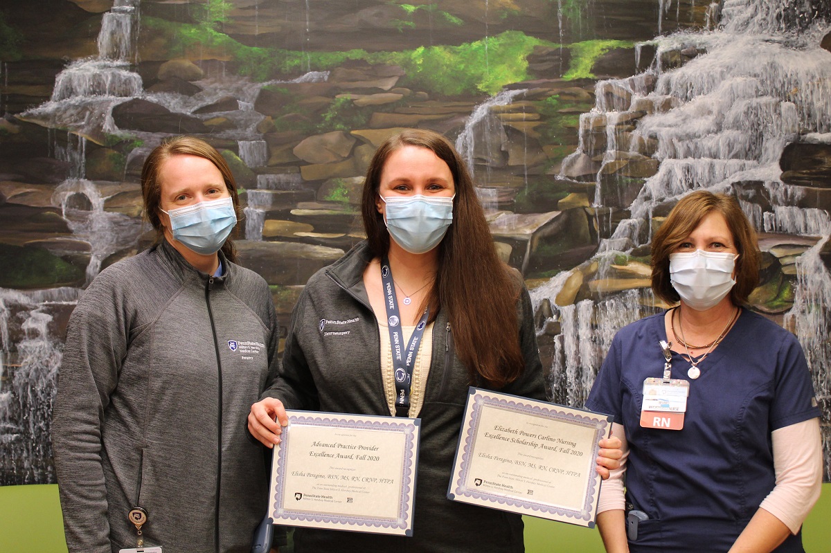 Elisha Peregino holds two plaques flanked by two of her colleagues in front of a background painting featuring waterfalls.