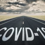 A roadway stretches into the horizon. On the pavement are written the words “COVID-19.”
