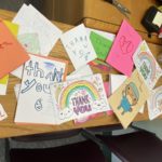 More than a dozen handmade cards cover a wooden desk. Some have pictures of rainbows, doctors and hearts and words that say “kind,” “giving,” “thoughtful” and “hero.”