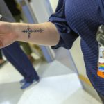 Female chaplain, with focus on name badge and cross tattoo on her arm.