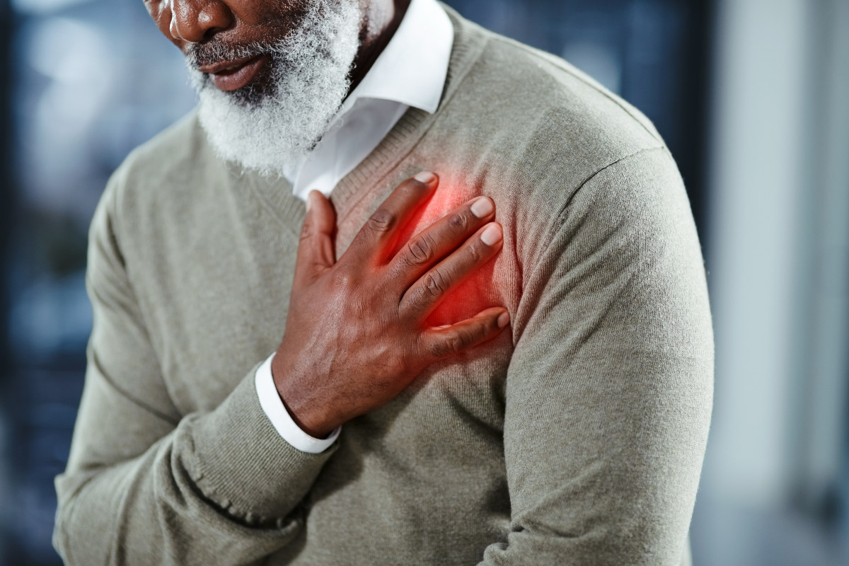 A man wearing a sweater places his right hand over his heart, apparently in chest pain.