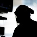 A silhouette of a medical care provider wearing protective gear, including a face shield and mask, while working in a patient room.