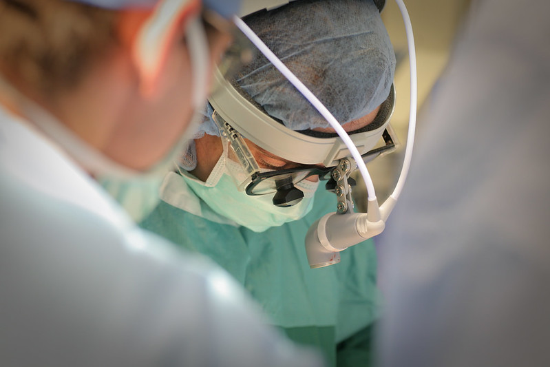 A surgeon and other staff lean over an operating table.