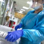 Health care provider wearing personal protective equipment working with medication. Focus on hands and medication.