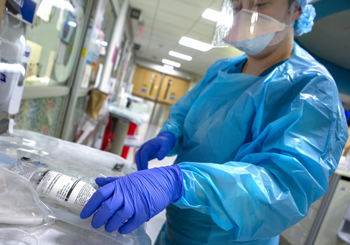 Health care provider wearing personal protective equipment working with medication. Focus on hands and medication.