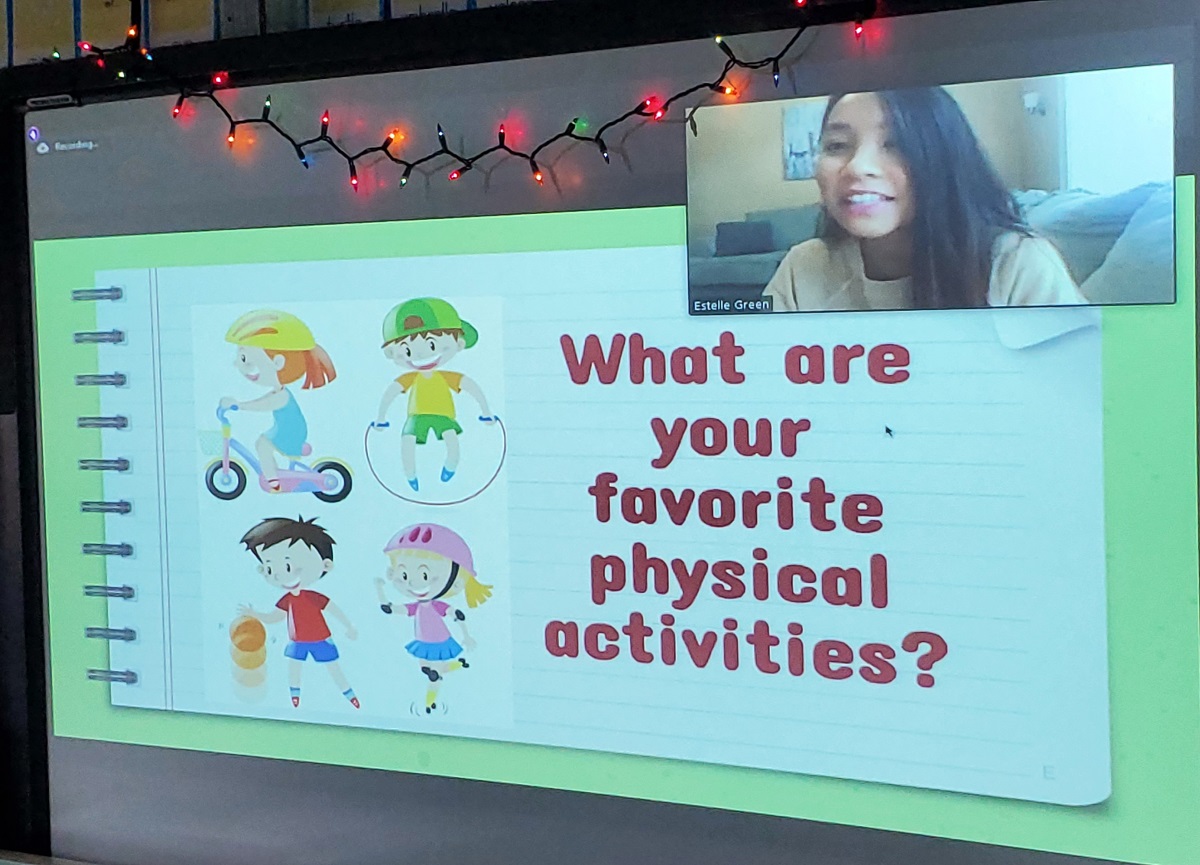 A computer screen shows Estelle Greene in a window in the upper left corner. The screen features the words “What are your favorite physical activities?” with animated characters