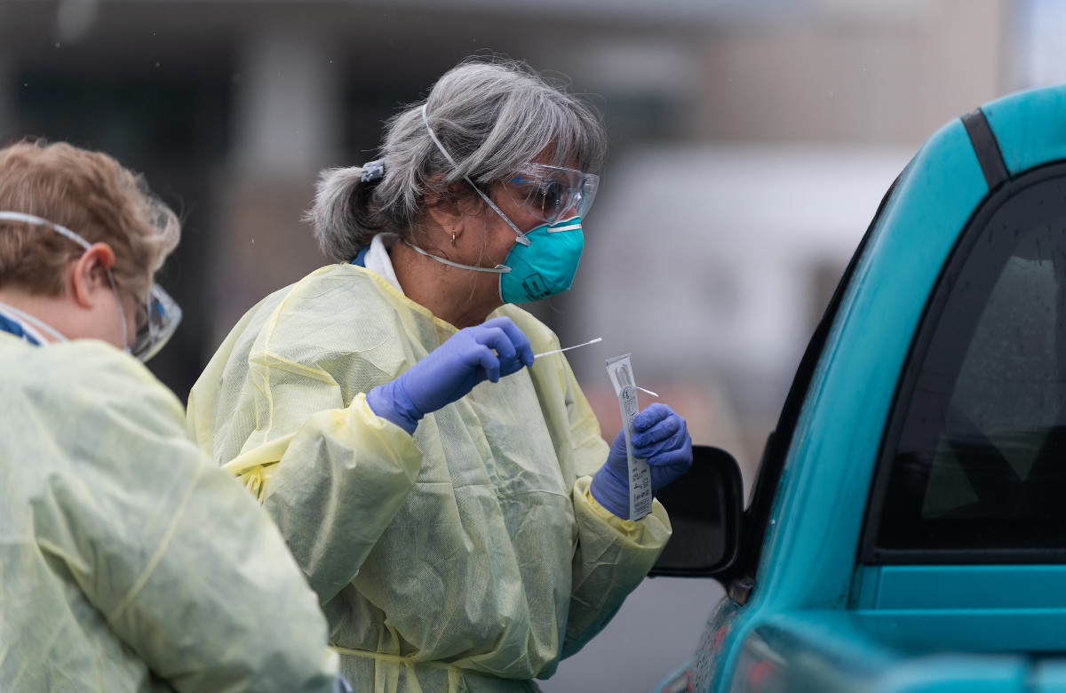 A nurse in full personal protective equipment administers a COVID-19 test at a drive-through testing location