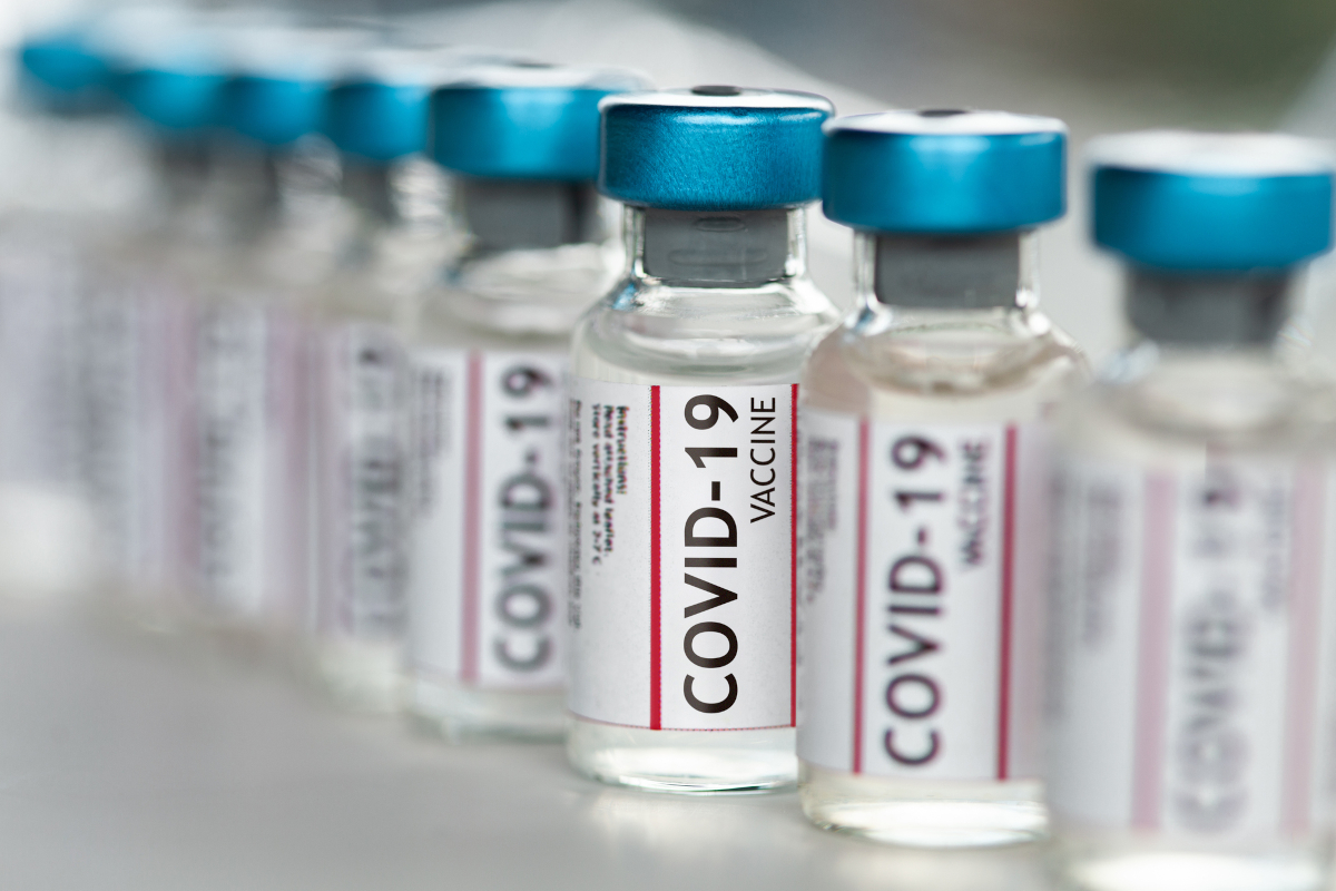 Several small bottles labeled “COVID-19 vaccine” are side-by-side on a table.
