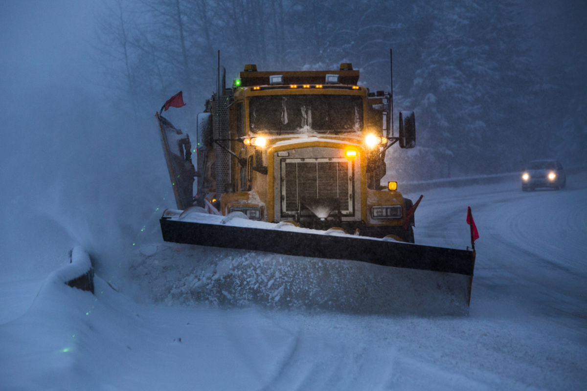 A plow cleans snow off a road at night.