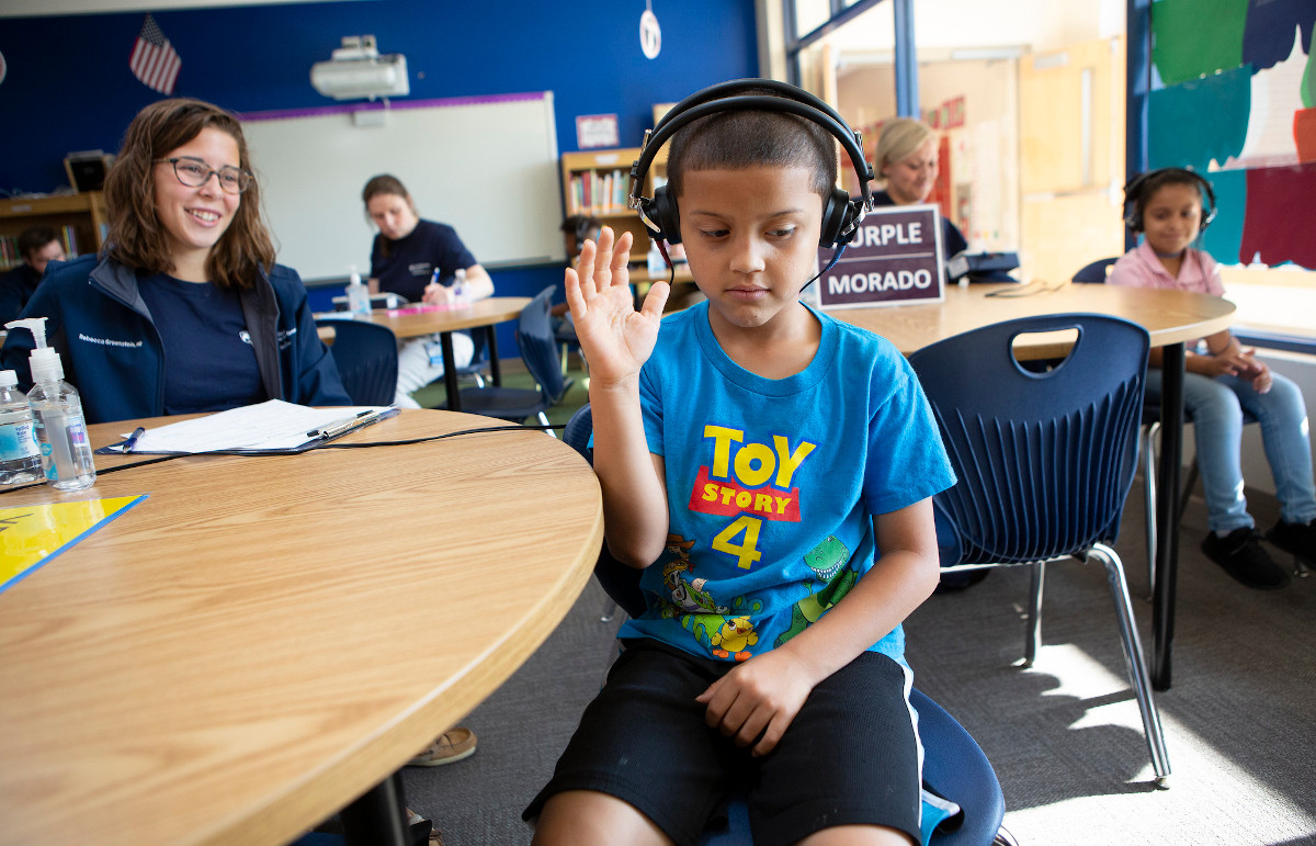 A boy wearing headphones raises his arm while doing a hearing test