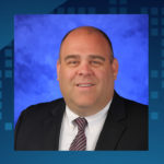 Scott Mickalonis' head shot is in the middle of a blue banner and a stone sculpture of the Nittany Lion is on the right.