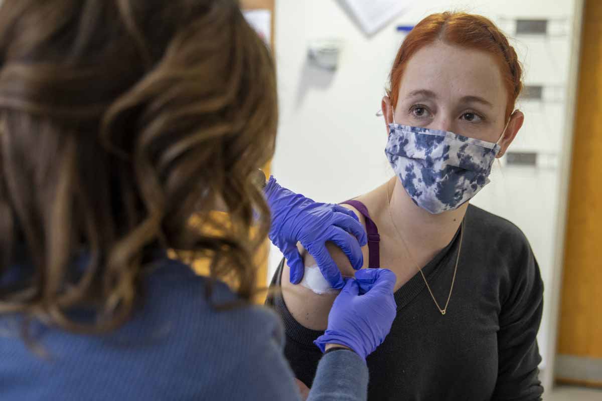 Una enfermera coloca una venda en el brazo derecho de una mujer después de haberle dado una inyección.
