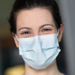 Close-up photo of a woman in a facemask, smiling.