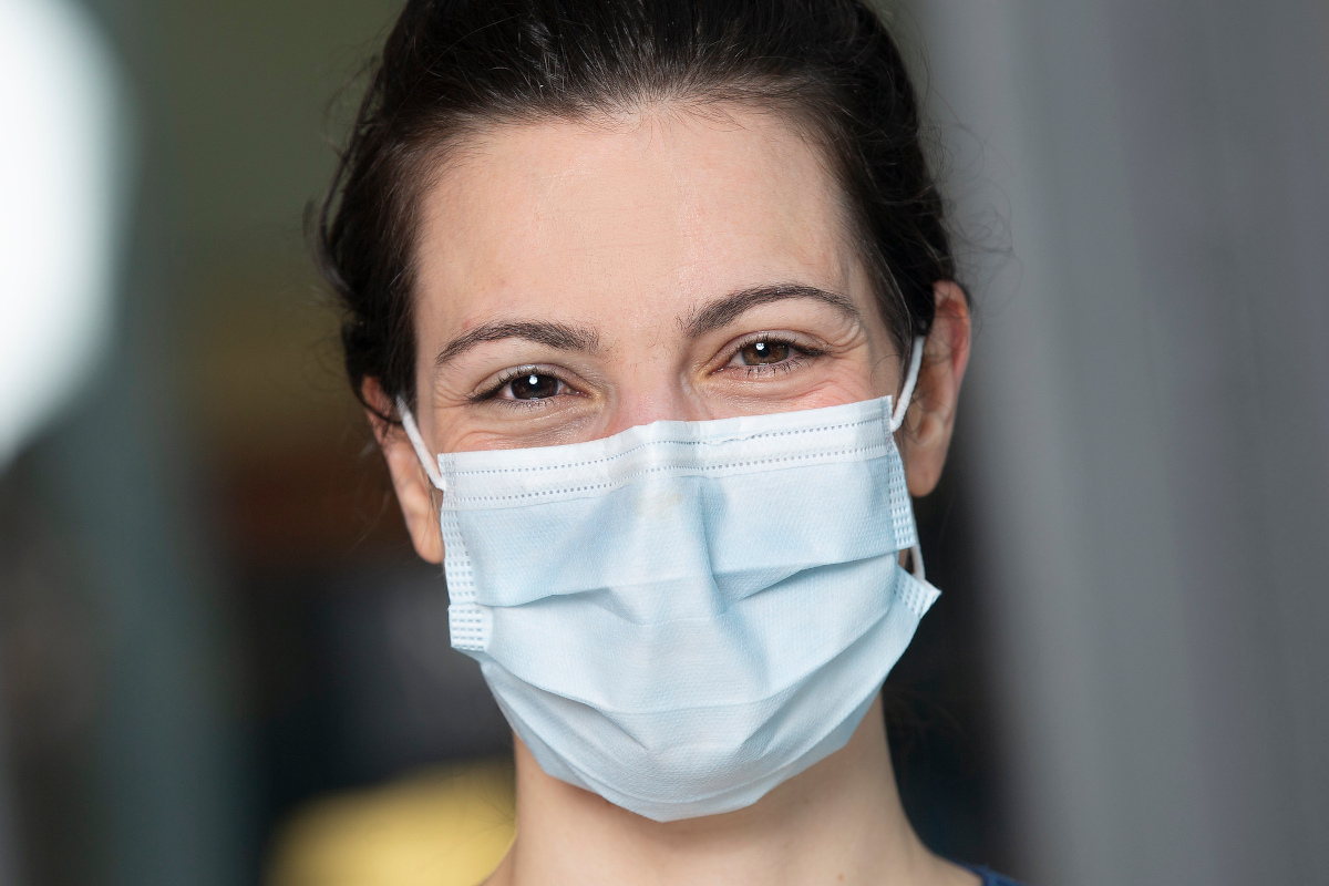 Close-up photo of a woman in a facemask, smiling.