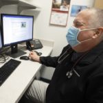Exercise physiologist Mike Zehner laughs while conducting a virtual cardiac rehabilitation visit on a computer screen with patient Brian Welsh.